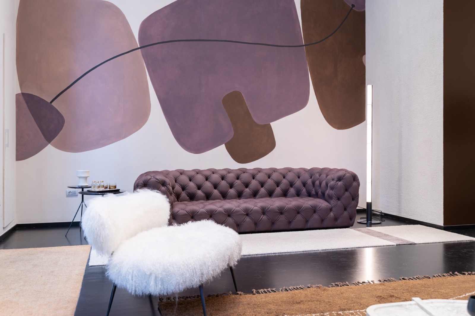 Divano capitonné viola e poltrone in pelliccia bianca davanti a una parete decorata, showroom Baxter