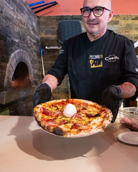 Pizzaiolo di Piccinni28 mostra una pizza con prosciutto, burrata e pistacchio davanti al forno